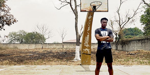 CEBL player, Kobe McEwen, stands in front of a basketball net on a basketball court in Honduras. 