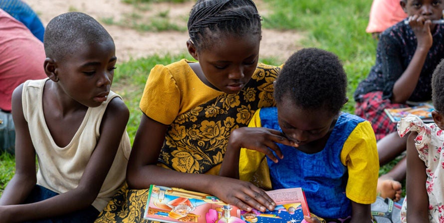 In the DRC, a girl reads a book for two younger children while others sit around them.
