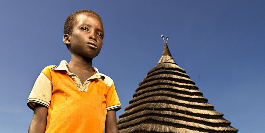 A young boy standing in front of a straw hut in Sudan