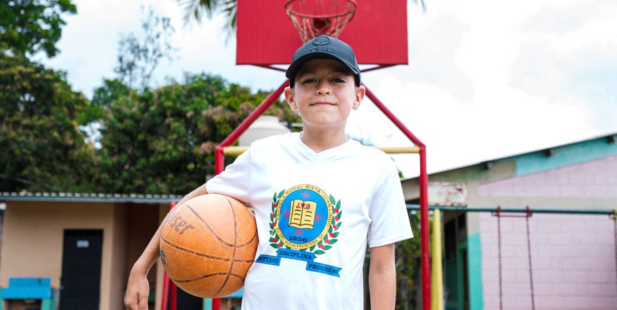 A young boy smiles while holding a basketball in Honduras. 